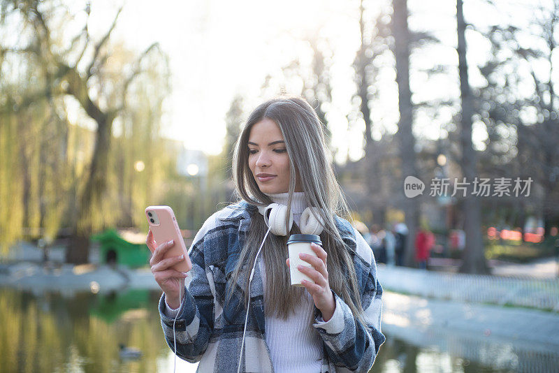 快乐的年轻女子走在城市的街道上，用她的智能手机