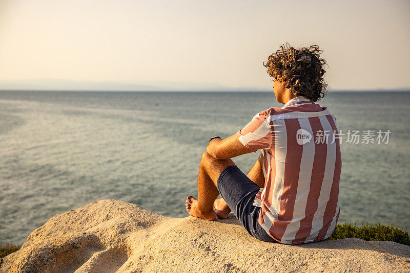 宁静的白人男子欣赏日落从岩石海滩