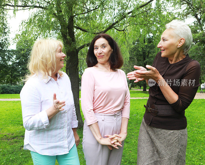 快乐的退休妇女在公园聚会。公园里的两位女性朋友向第三位女性表示祝贺。