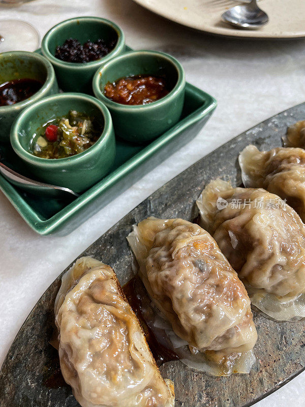 特写图像的餐厅餐桌设置，盘混合馄饨(中国饺子)充满鸡肉，猪肉或鸭，模子充满中国蘸酱，重点在前景