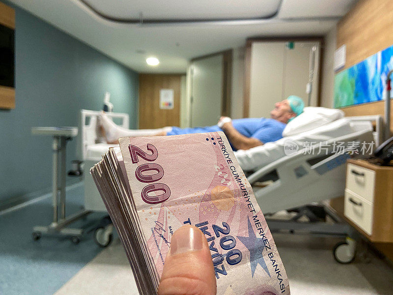 医疗保健成本。医院病房里，一名病人躺在病床上，手里拿着土耳其货币。有医院背景的手拿着土耳其钱