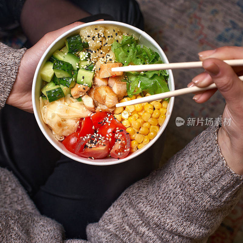 清洁饮食的饮食理念。一个正在吃午饭的女人手里拿着一碗牛油果鸡肉，装在可取出的纸盒里。特写，复制空间，俯视图