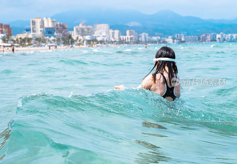 一个孩子，一个七岁的女孩，在海里洗澡。从后面看。