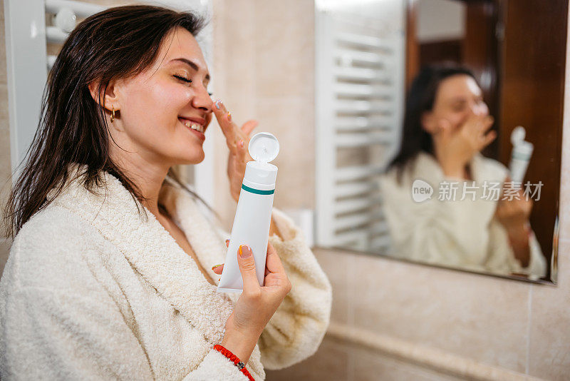 年轻女子在浴室的镜子里给脸上涂保湿霜