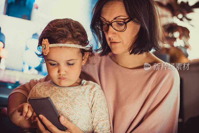 母亲教她的小女儿如何使用智能手机。