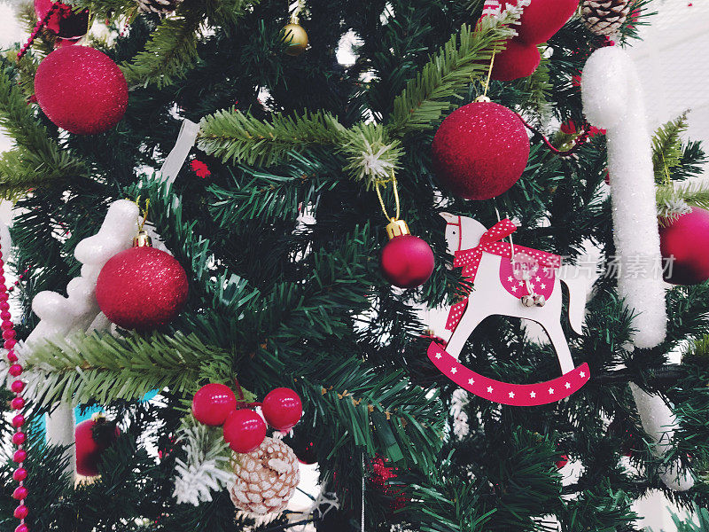 圣诞树上有装饰品、圣诞球和玩具。红白挂饰。美丽的球，明亮的浆果和球果。雪糖棒。玩具-摇马