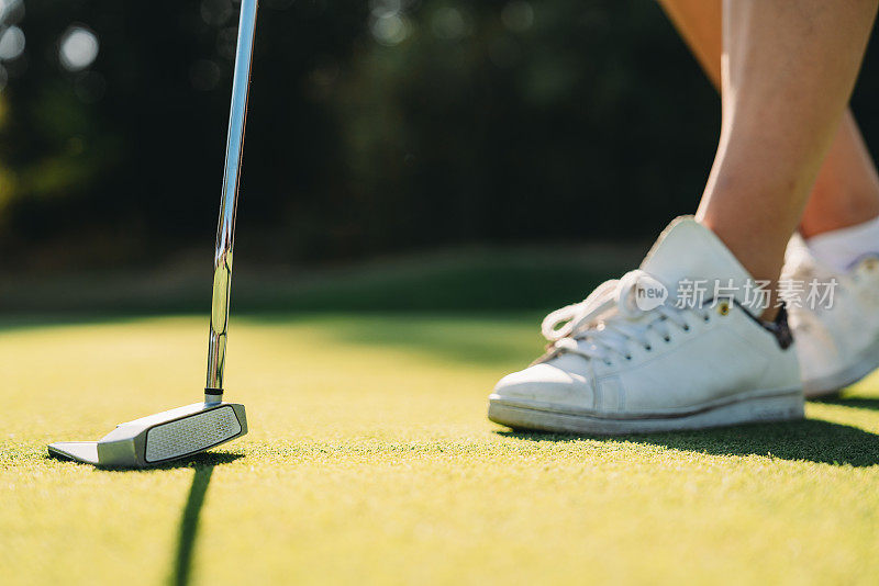 绿地上一位女高尔夫球手的球鞋和球杆的细节