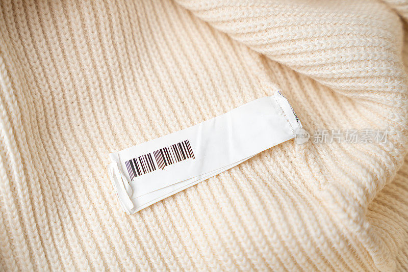 服装标签特写，空白服装标签上的米色针织衫