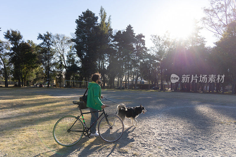 一个年轻的墨西哥人，带着他的自行车和狗在公园里散步