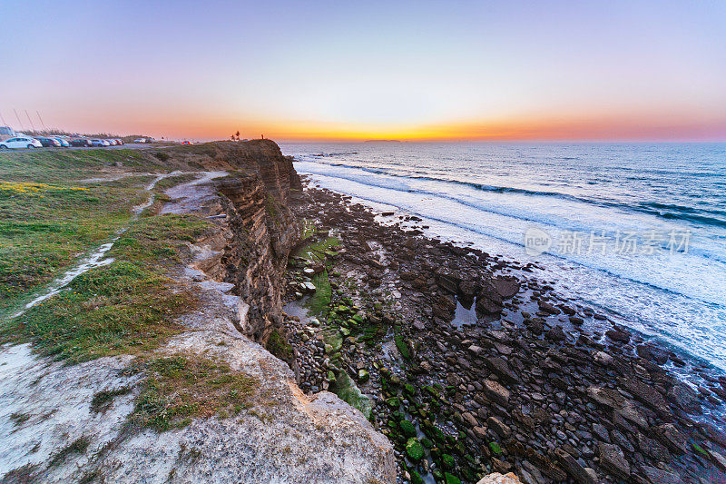 海岸悬崖在日落:鲜艳的色彩，岩石地形，海浪，和遥远的地平线捕捉在黄金时间。Peniche,葡萄牙。