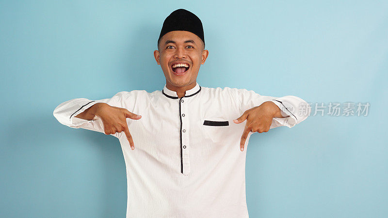 一名穆斯林男子用手指向下指向自由空间，在蓝光背景下为广告隔离的快乐表情