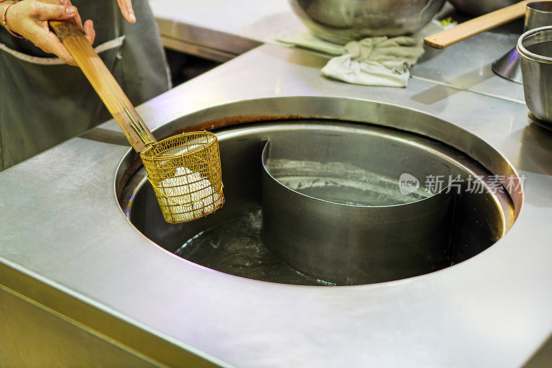 图为一名厨师在沸腾的锅里煮面条，准备在街边小吃店做汤面。