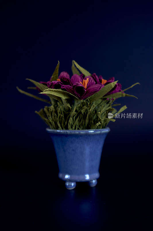 黑色背景的蓝色花瓶里的纸花