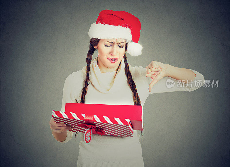 年轻女子戴着红色的圣诞老人帽打开礼物，对她收到的东西很不高兴，表现出不满