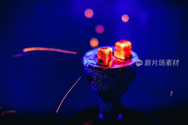 水烟与发光的红色余烬和飞溅的火花在碗在蓝色的背景