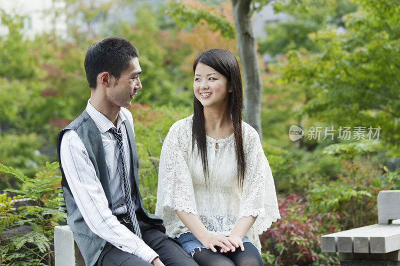 浪漫的年轻日本夫妇一起坐在公园长椅上