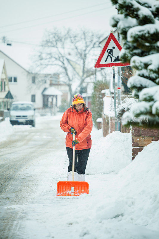 一个成熟的女人在清扫屋前的积雪