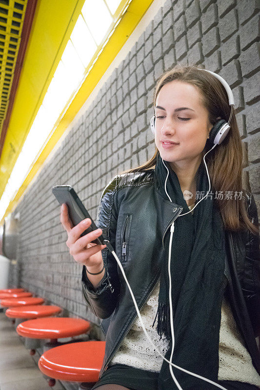 在地铁站用智能手机听音乐的美丽女人