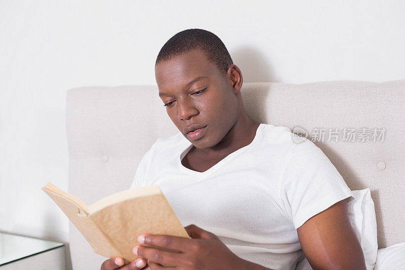 微笑的男人坐在床上看书