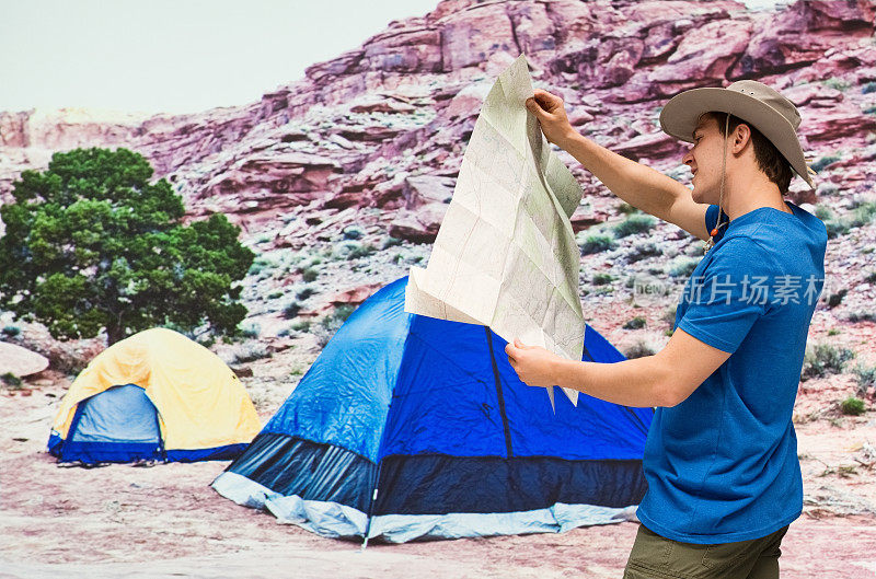 一个微笑的男人拿着地图站在帐篷前