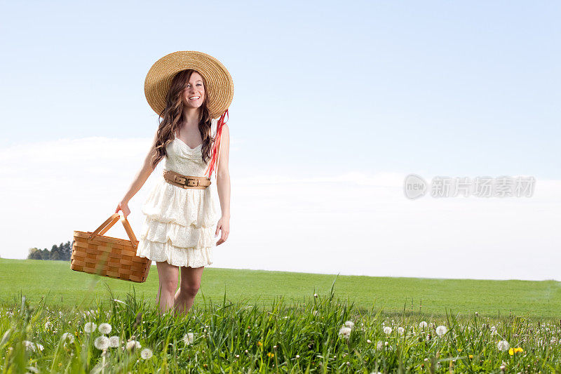 带着野餐篮走在草地上的年轻女子