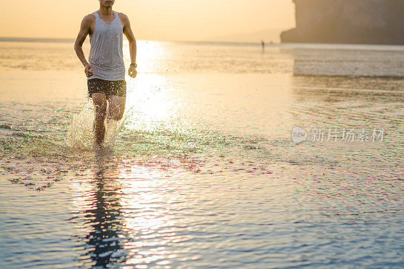 年轻的亚洲男子在海滩上奔跑，夕阳为背景