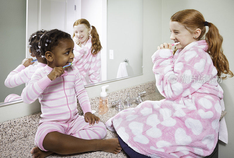 两个孩子(姐妹)坐在镜子前一起刷牙