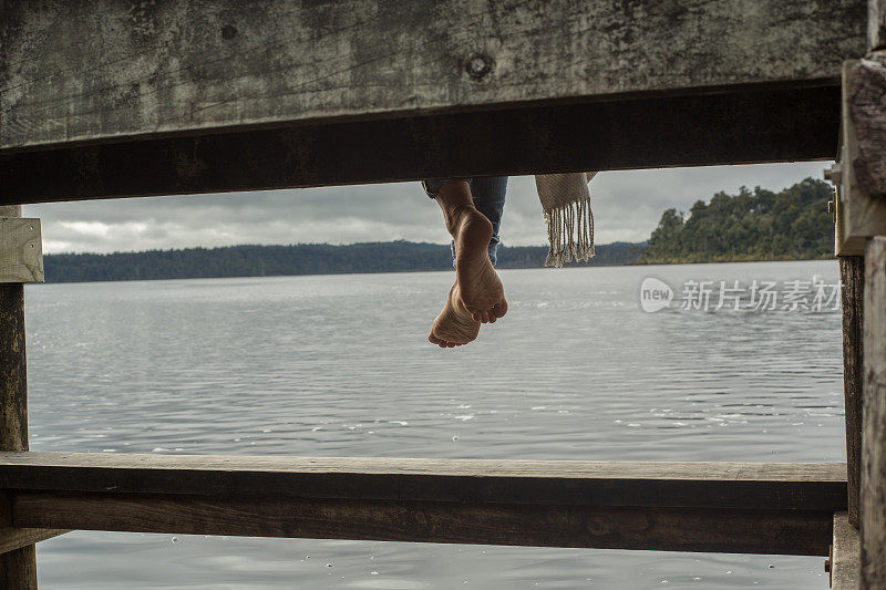 女人的双脚悬在湖面上的木码头上