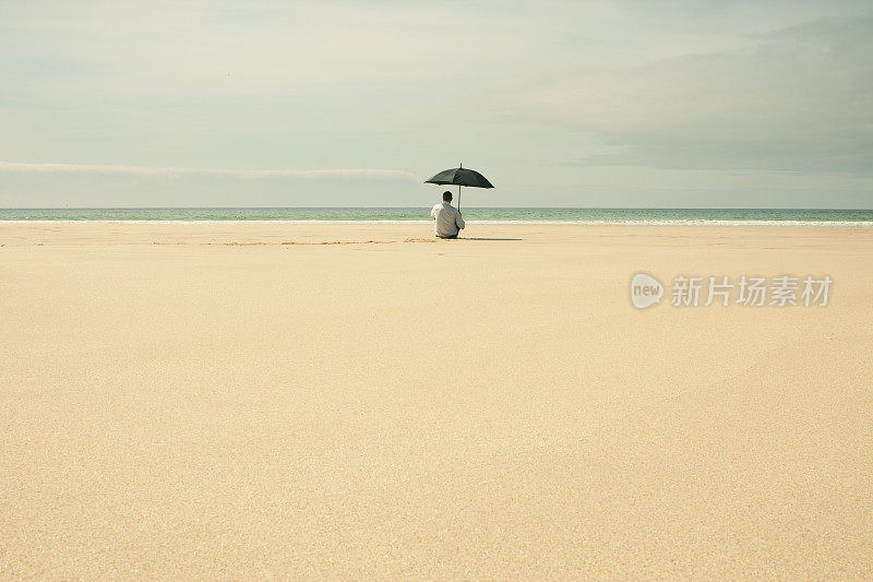 一个男人坐在荒芜的海滩上，手里拿着伞