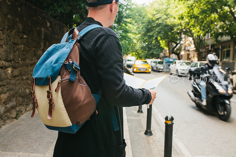 一个背着背包的年轻男性游客正在一个大城市里看地图。的旅程。观光。旅行。