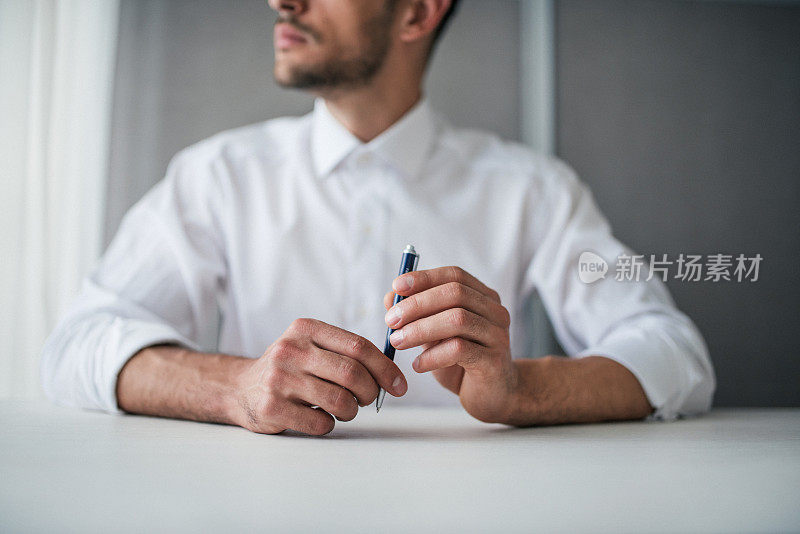 商业特写帅气的商人手拿一支笔。思考着，看着窗户。