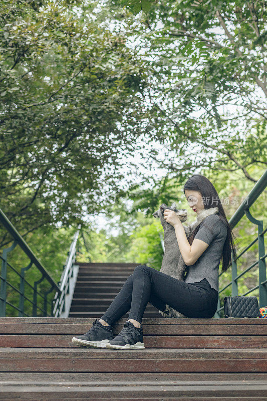 美丽的女主人拥抱她可爱的雪纳瑞在人行桥