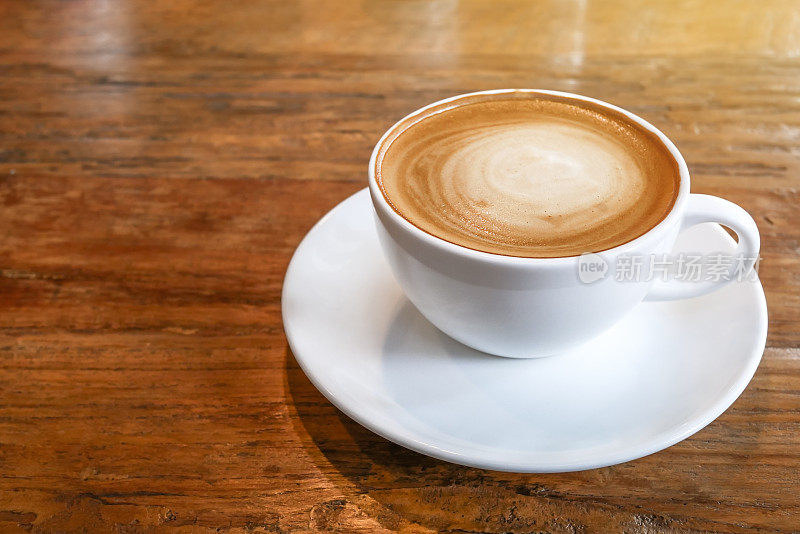 热咖啡卡布奇诺杯与螺旋牛奶泡沫木桌子的背景。