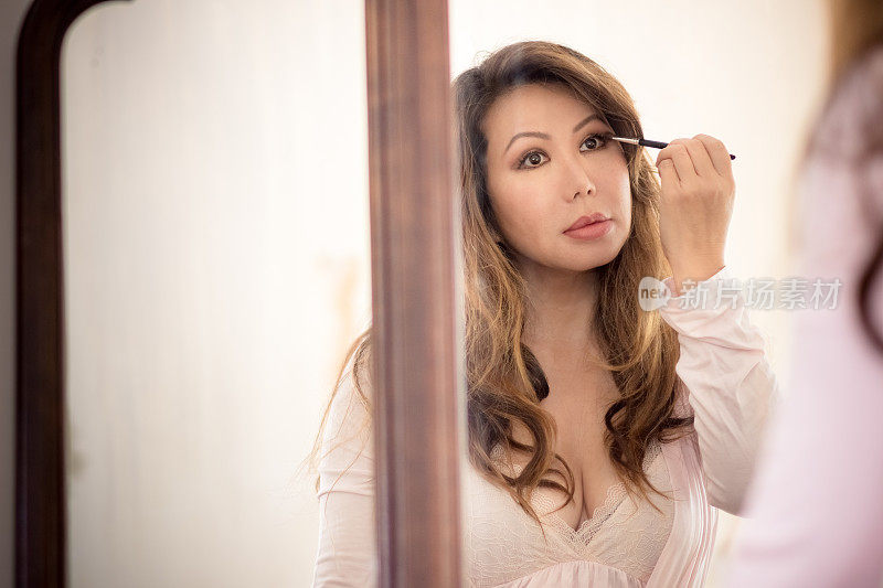 美丽的亚洲女人看着古董镜子上眼妆