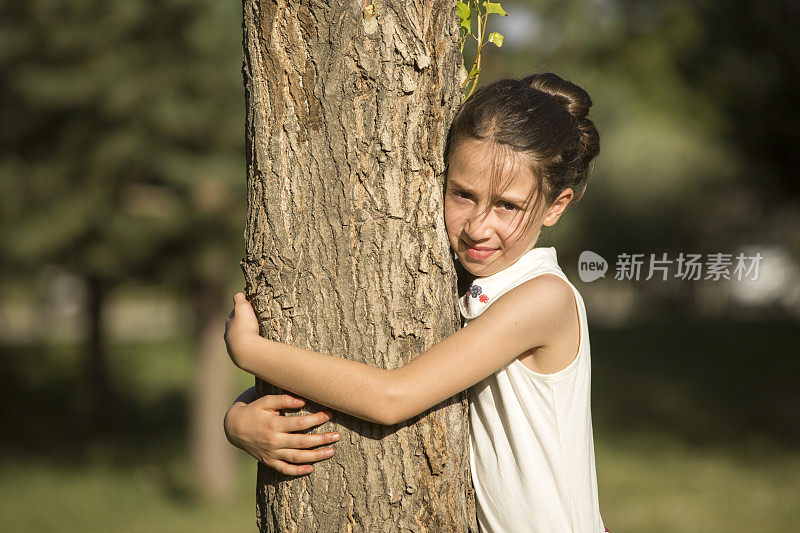 美丽的小女孩微笑着拥抱着树干
