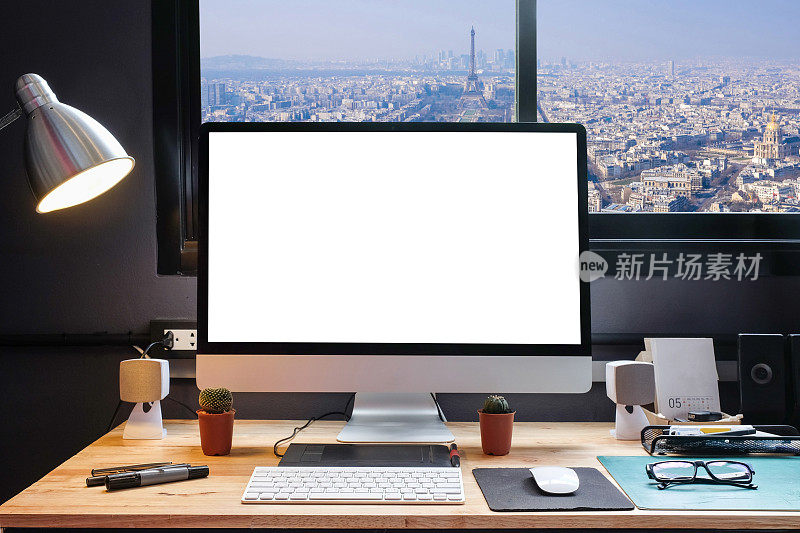 平面设计师的工作空间配备了一个手写板，一台电脑和白色背景的文字与美丽的巴黎城市从窗口