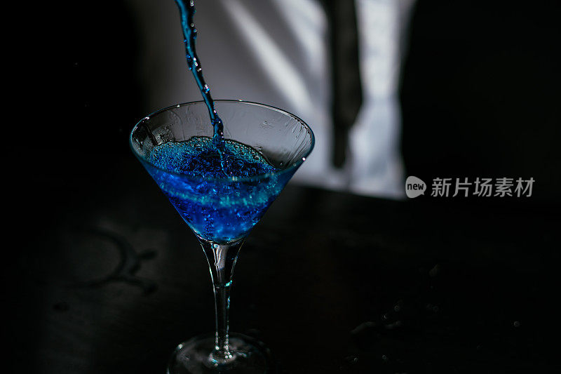 调酒师将蓝色鸡尾酒倒入马提尼酒杯