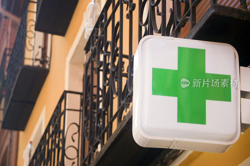 药店的标志，街道上的绿色十字，建筑物有铸铁阳台。