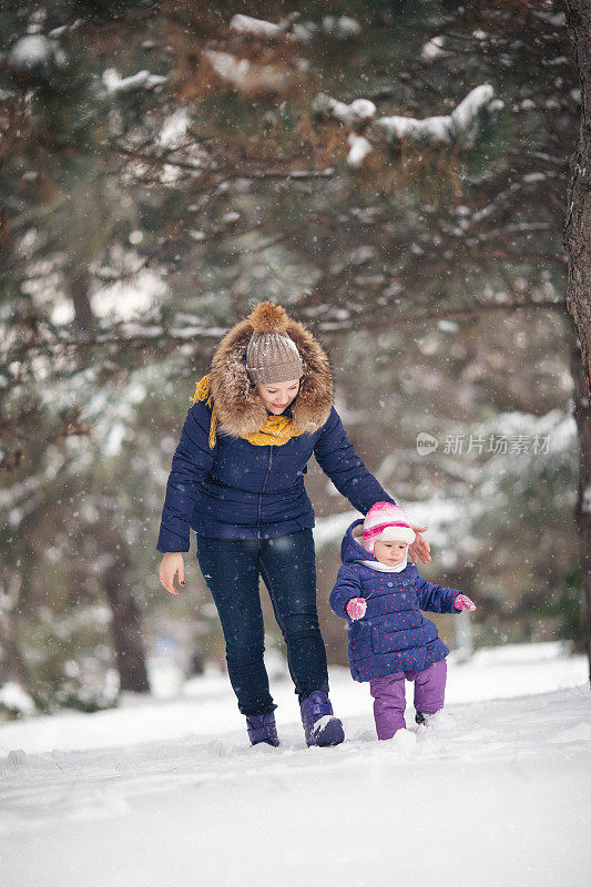 妈妈和她的宝贝女儿在雪地里行走