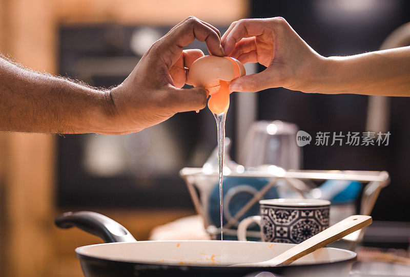 一对面目全非的夫妇在准备用平底锅煎鸡蛋之前敲开鸡蛋。