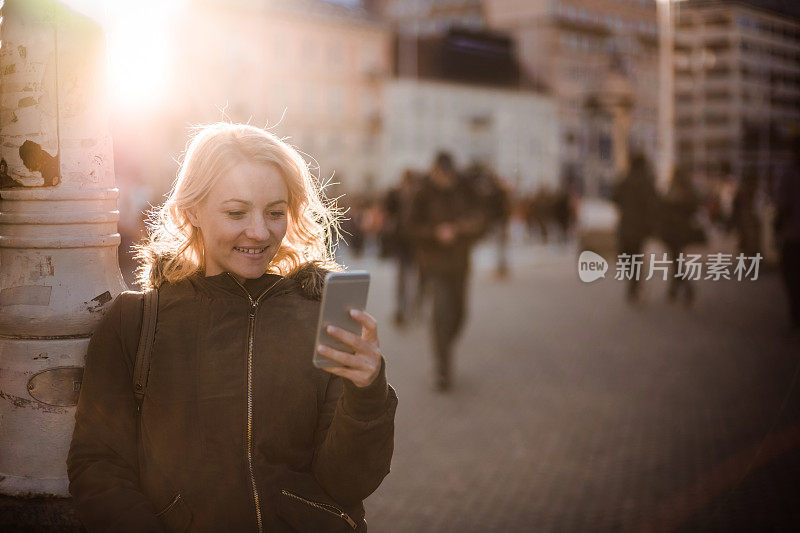 年轻快乐的女人在城市里用她的智能手机发短信。