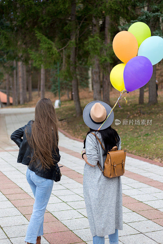 两个女性朋友拿着彩色气球在公园里散步