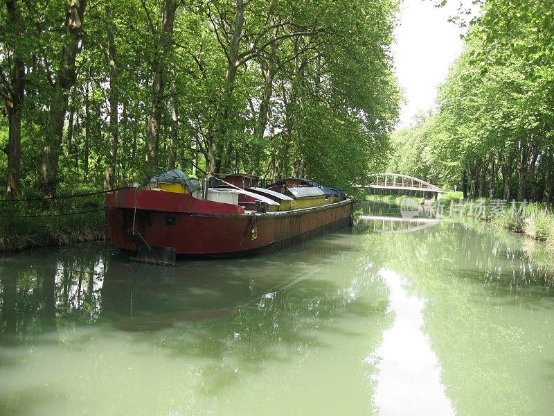 法国南部，加隆河旁的运河，河岸上有船只和树木