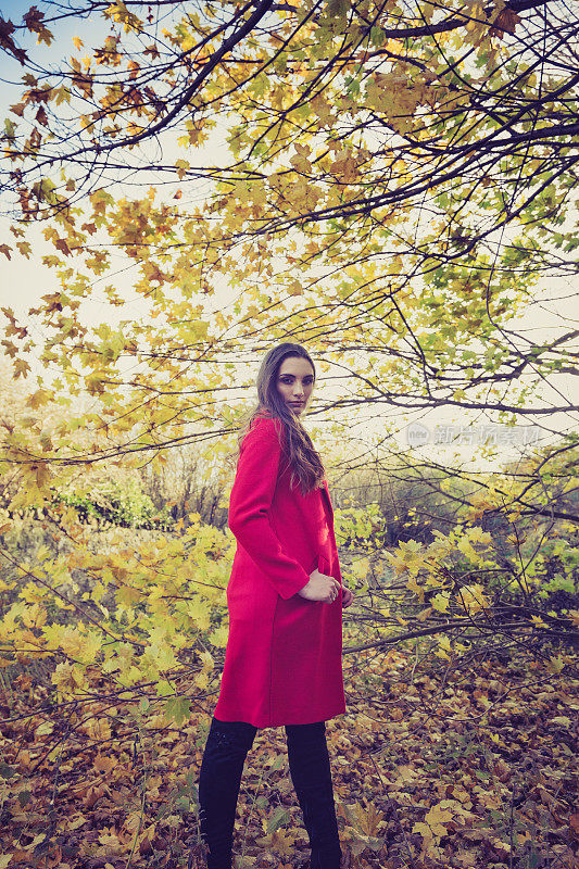 一个年轻女子在森林里转过身来，穿着一件红色的长夹克。