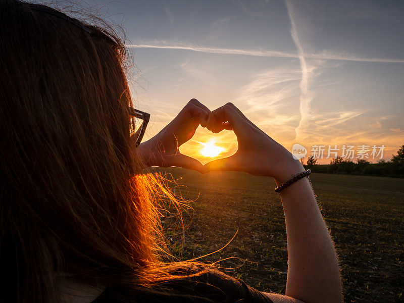 年轻女子在夕阳下用手画出一颗心