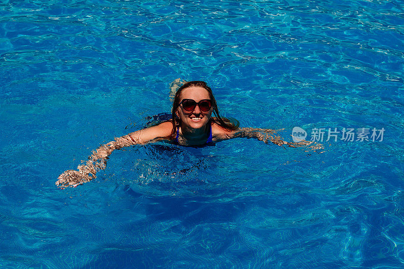 一个戴着墨镜的年轻女子在游泳池里游泳