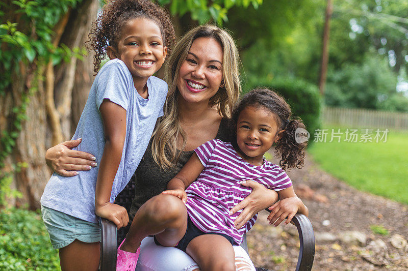 亚裔华人母亲和两个华裔和非裔美国人混血的女儿在一个绿色茂盛的后院里摆姿势拍照微笑和傻笑