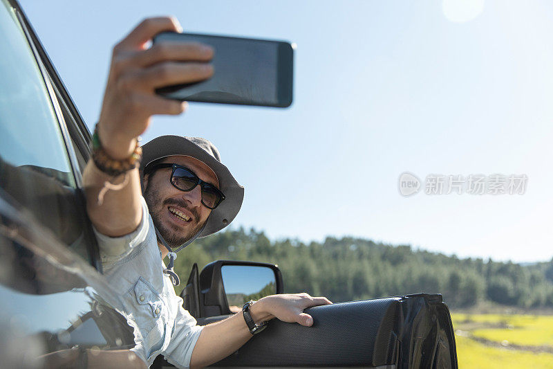 开车旅行时，一名男子一边自拍一边用智能手机发送信息