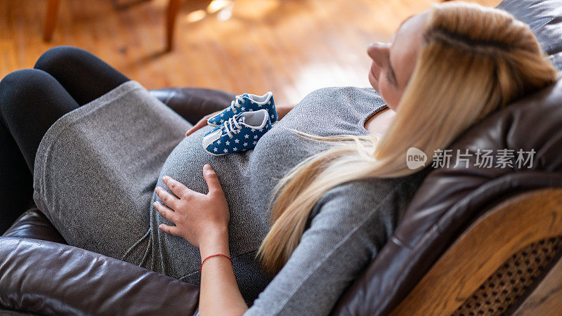 肚子上放着婴儿鞋的孕妇