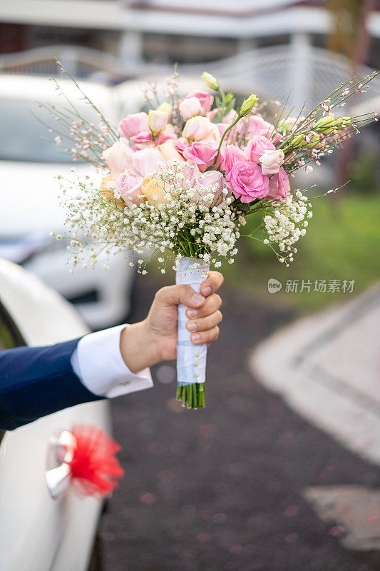 亚洲男子手捧花束从婚礼车